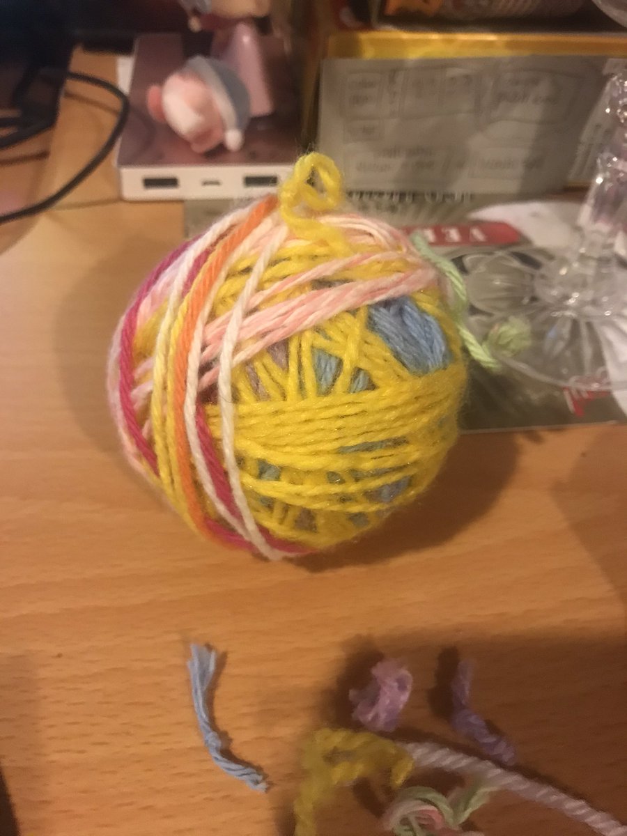 colourful pastel ball of yarn on a wooden desk with a copy of AOL online, kirby, and a cardboard piece with writing in the background. scrap yarn is in the foreground